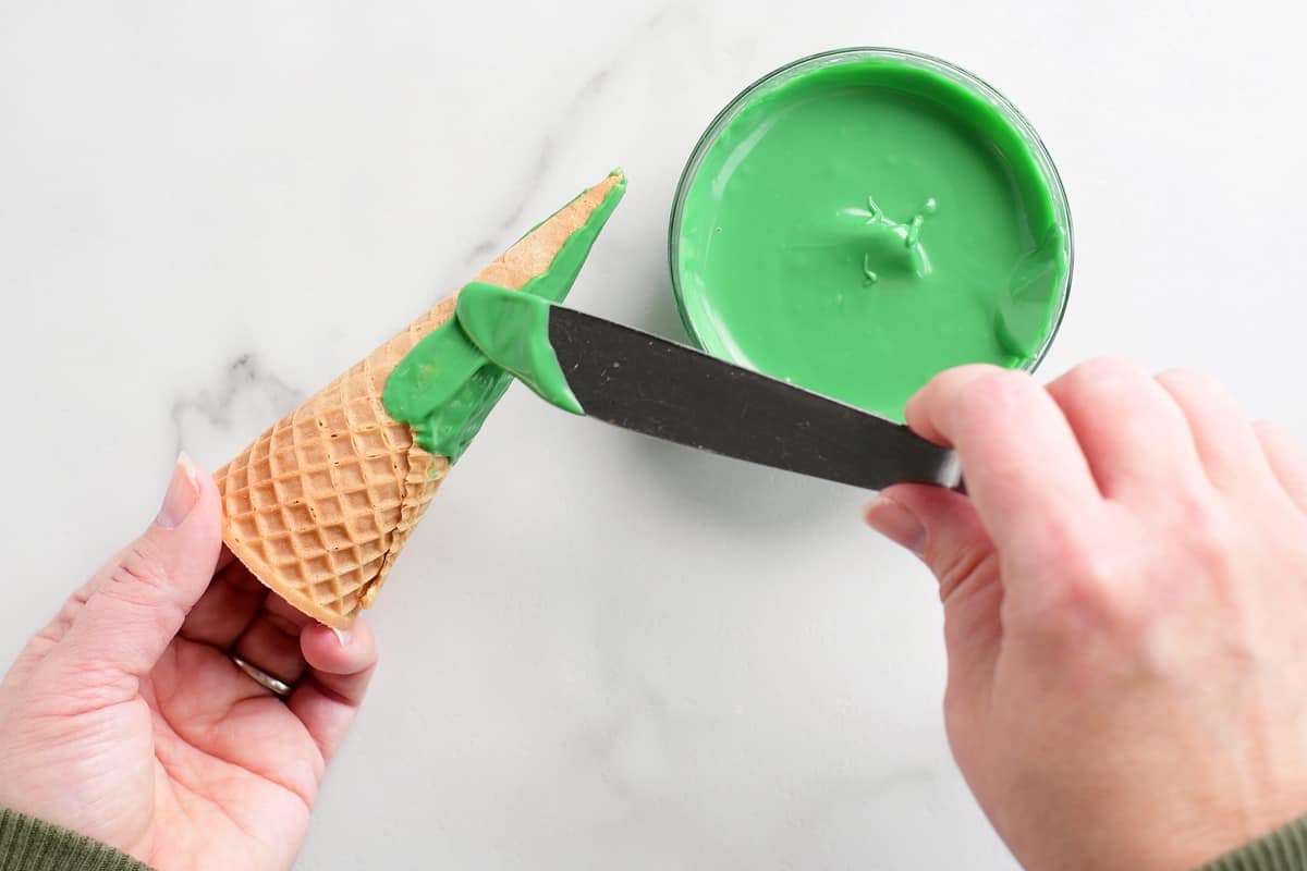 using a butter knife to apply green icing to an ice cream cone