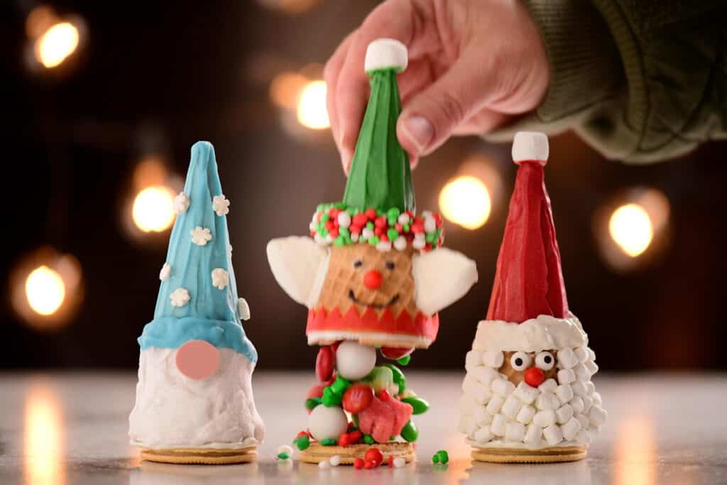 candy tumbles out of an elf Christmas cone as a hand pulls the top of the cone away from the cookie base