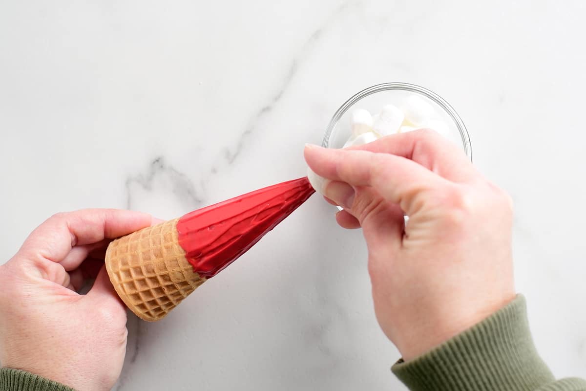 adding a small marshmallow to the tip of an ice cream cone that is frosted red