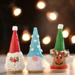 Christmas cones decorated as a Santa, Elf and Gnome set on a table in front of holiday lites