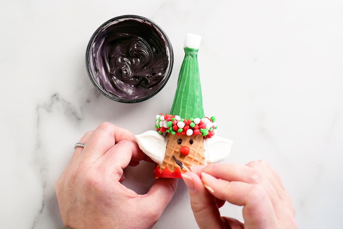 using a toothpick to draw a face on the elf Christmas cone