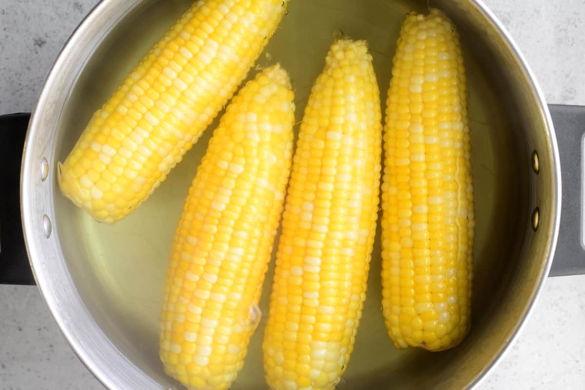 four cobs of corn in  a pot of water.