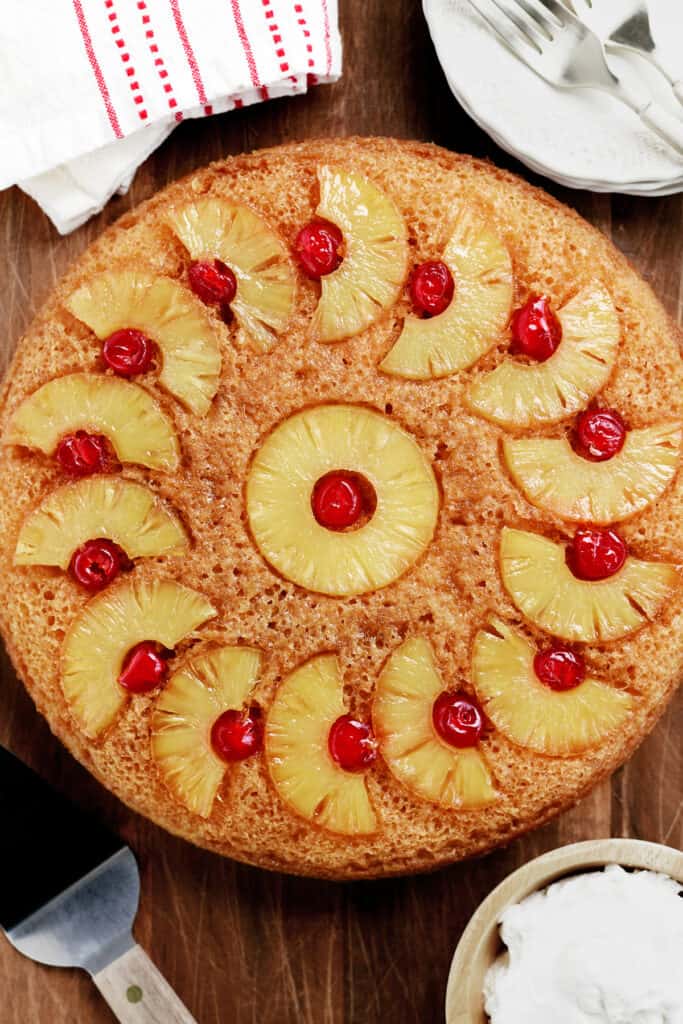 pineapple upside down cake, plates, forks and a serving utensil on a wooden surface