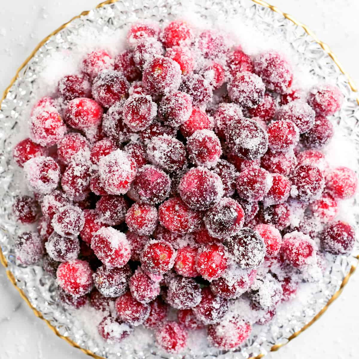 sugared cranberries in a pile on a gold rimmed plate