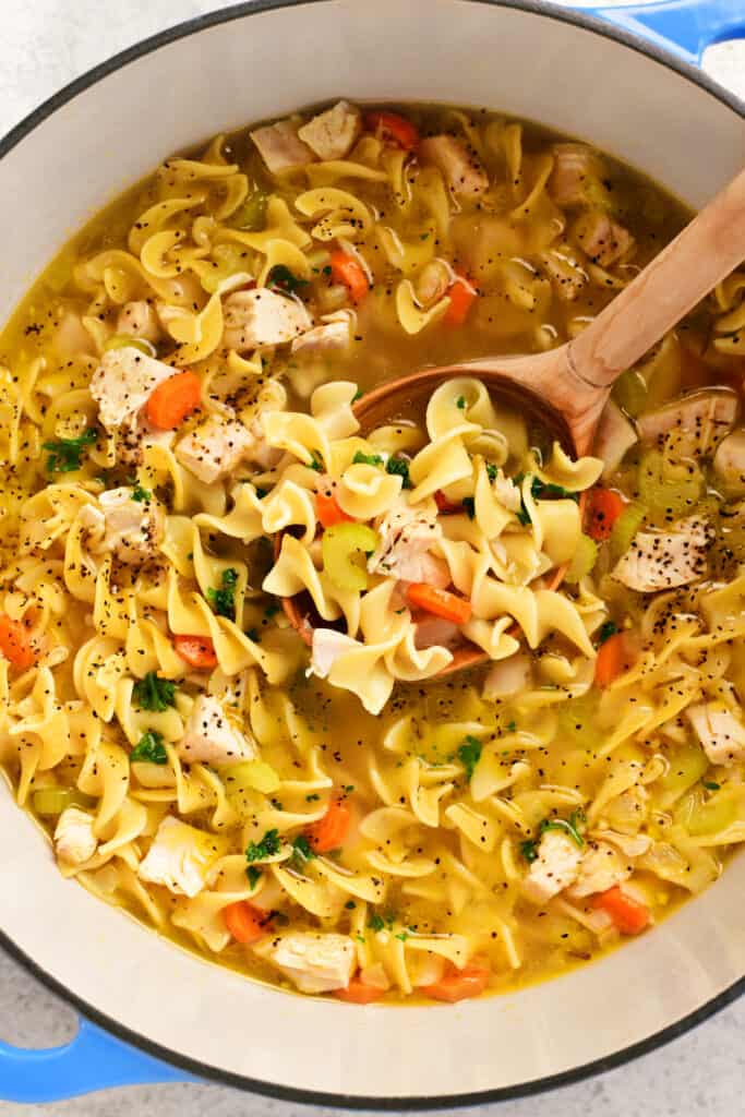 a wooden spoon in a pot of turkey noodle soup