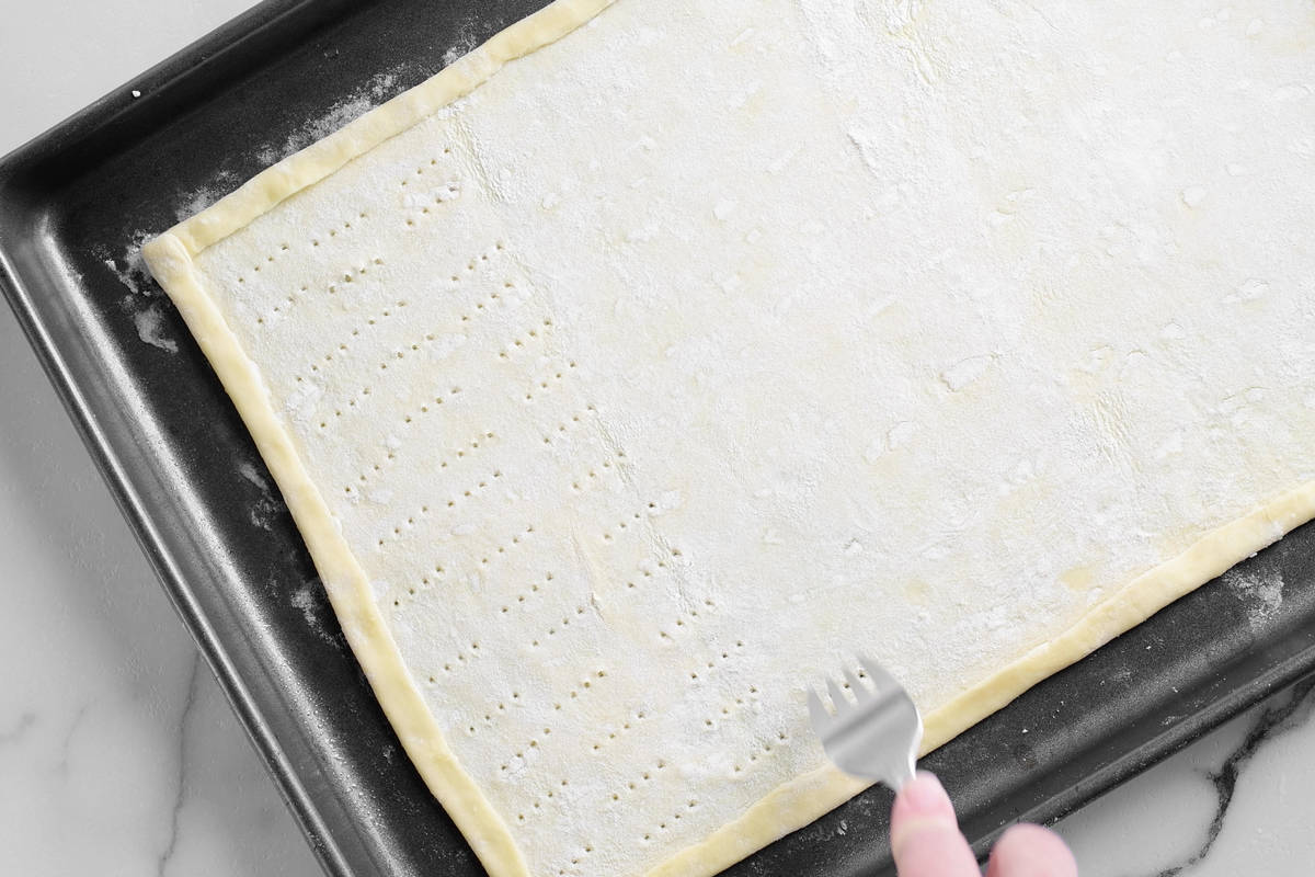 a hand using a fork to perforate the dough