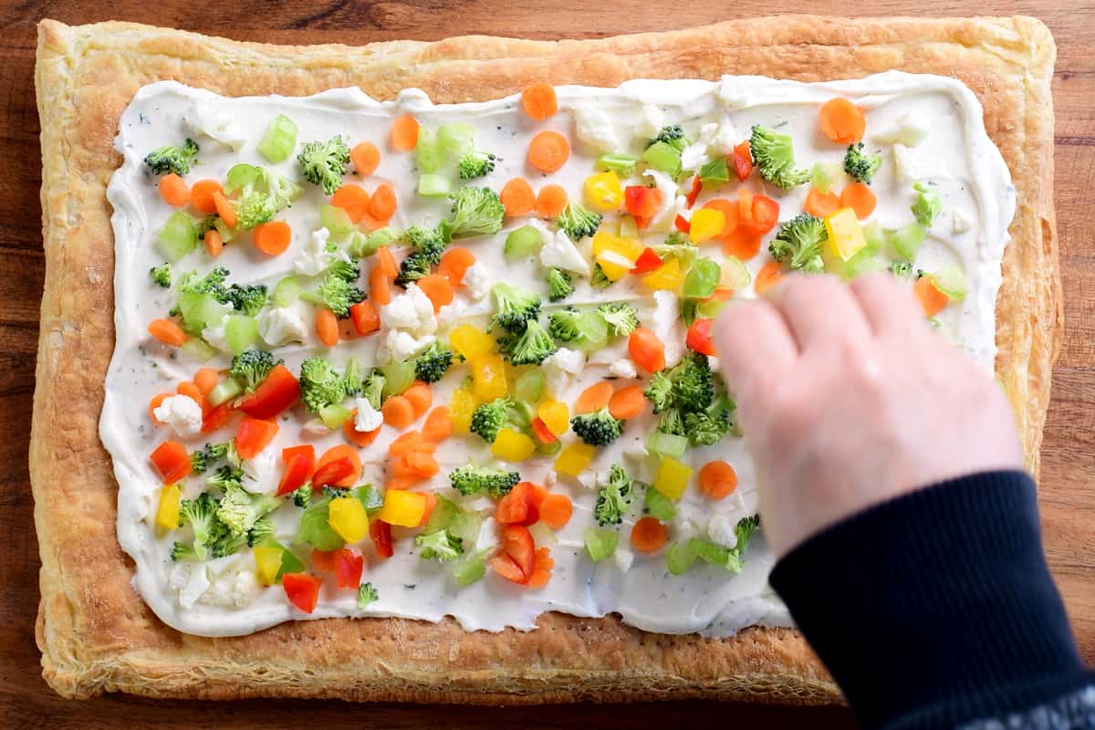 a hand adding veggie toppings to the pizza
