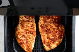 two cooked chicken breasts in an air fryer basket