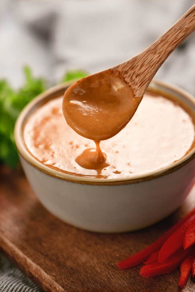 peanut sauce drizzling from a wooden spoon into a bowl