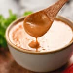 homemade peanut sauce drizzling from a wooden spoon into a bowl