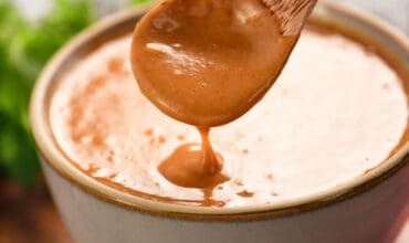 homemade peanut sauce drizzling from a wooden spoon into a bowl