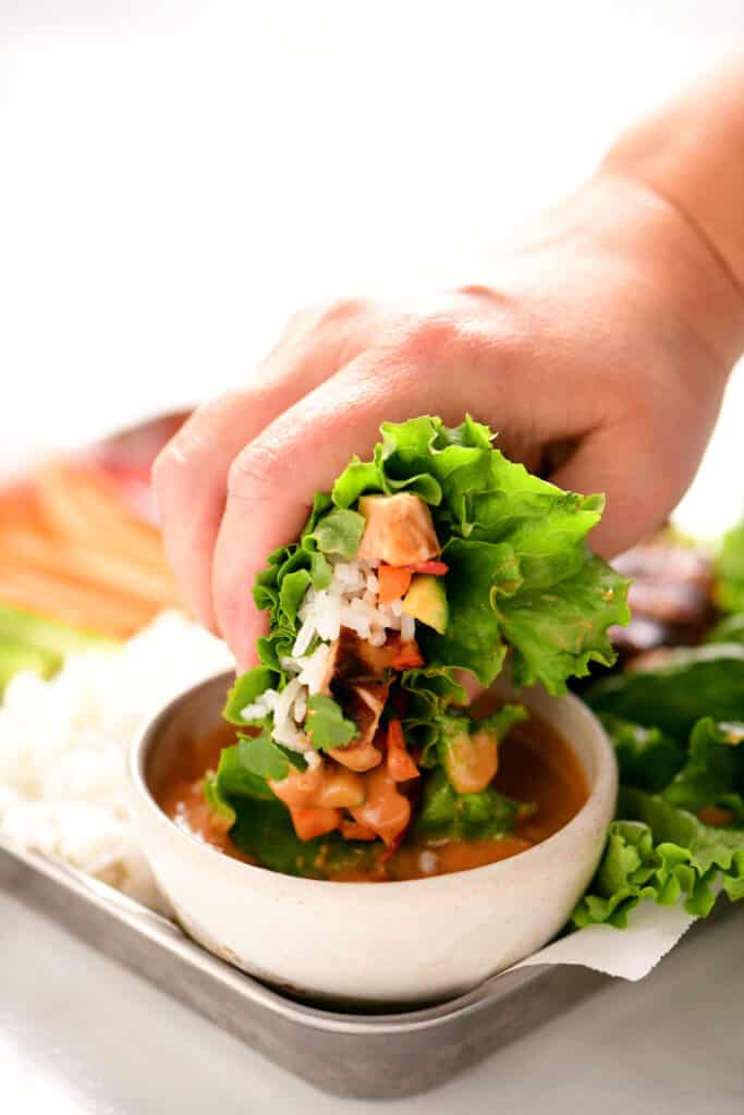 a hand dipping a chicken lettuce wrap in peanut sauce
