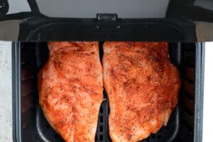 two uncooked chicken breasts in an air fryer basket