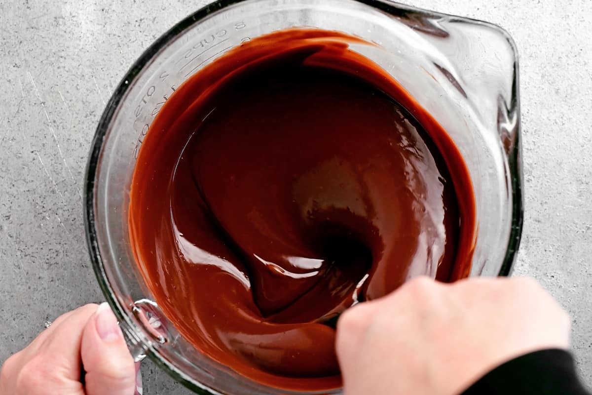 a hand stirring the melted chocolate mixture with a spoon