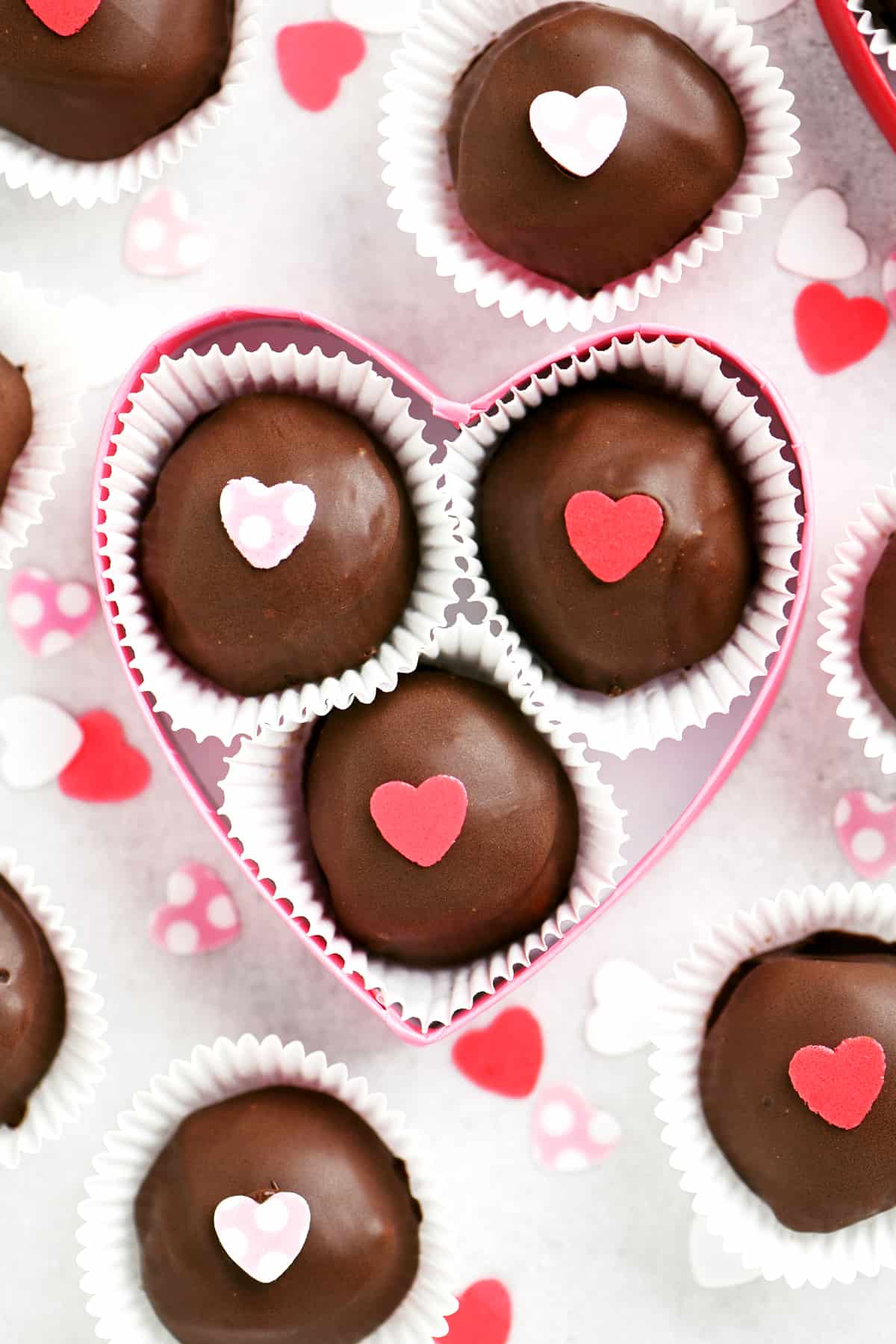 chocolate truffles in a heart shaped pink box surrounded by other truffles in paper cups