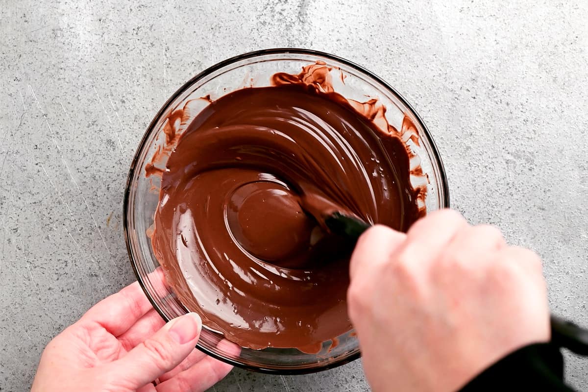 a hand using a rubber spatula to stir the melted chocolate