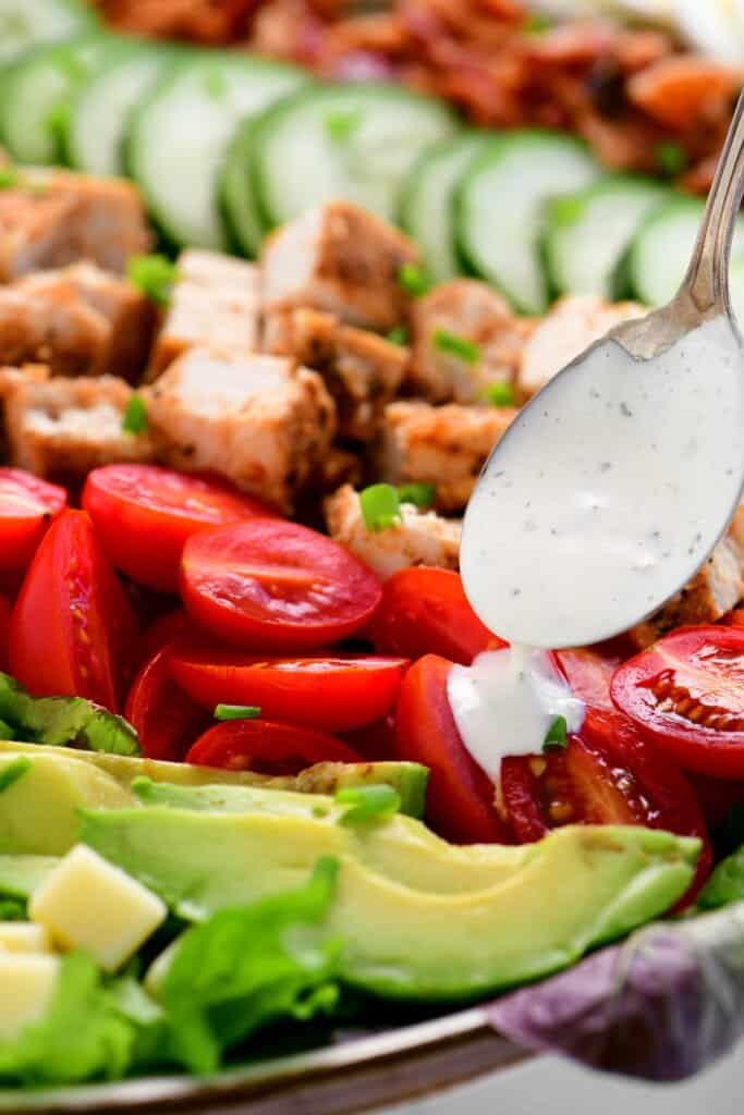 a spoon drizzles salad dressing on to salad toppings