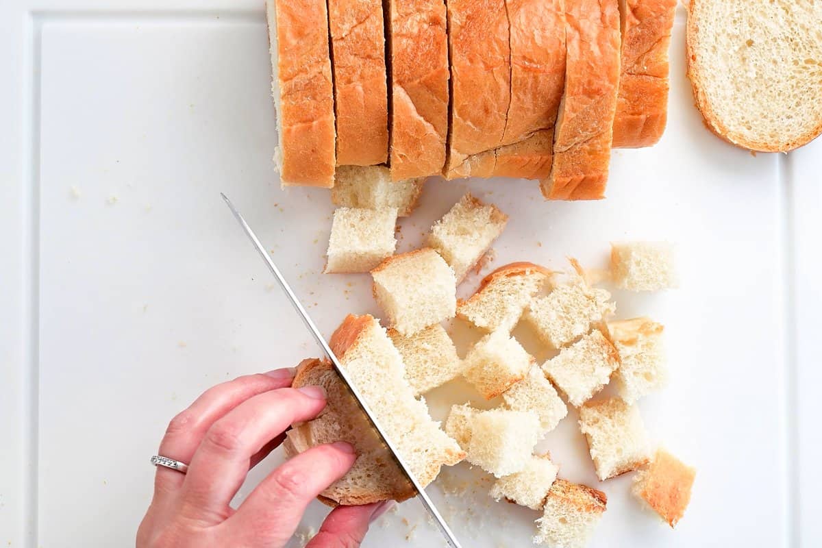 hands using a knife to cut bread in to small cubes