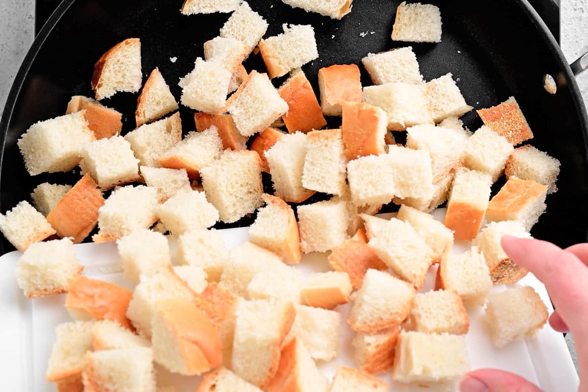 a hand adding many cubed pieces of bread to a pan