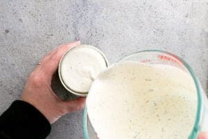 hands pouring ranch salad dressing from a mixing bowl into a glass jar