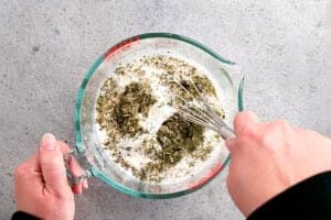 a hand using a whisk to stir seasoning into the salad dressing