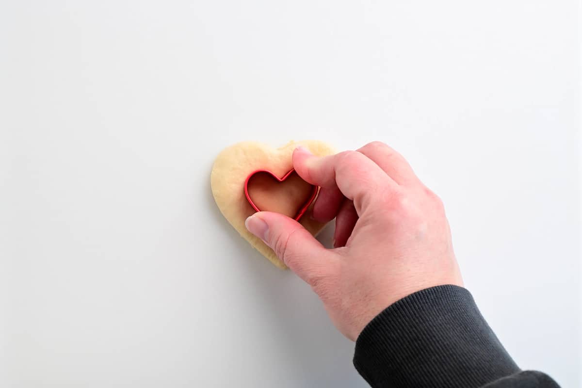 a hand pressing into the dough with a small heart shaped cookie cutter