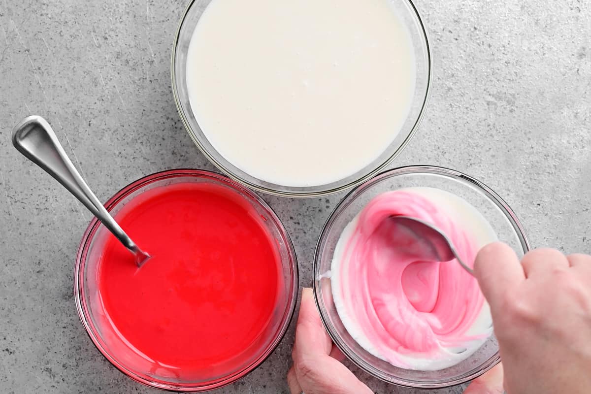 a hand stirring pink food coloring into the white donut glaze
