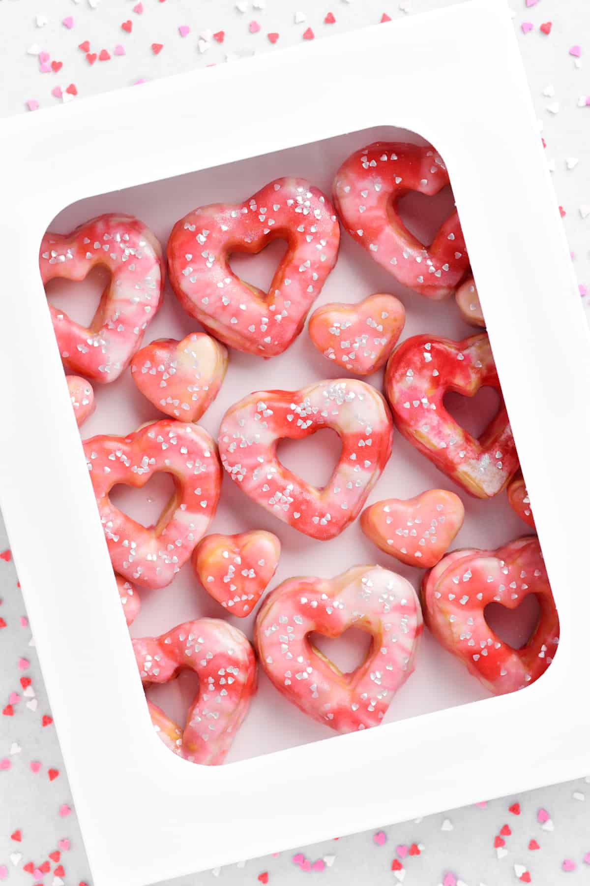 A white donut box with pink swirled valentines day donuts inside.