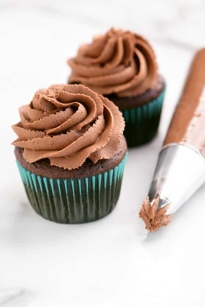 two chocolate cupcakes with buttercream frosting next to a piping tool