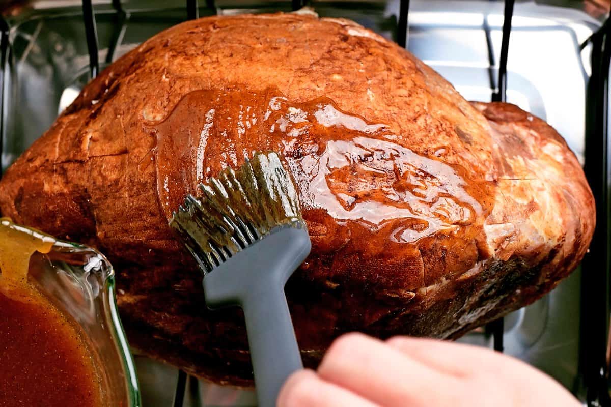 a hand adds the glaze to the ham with a brush