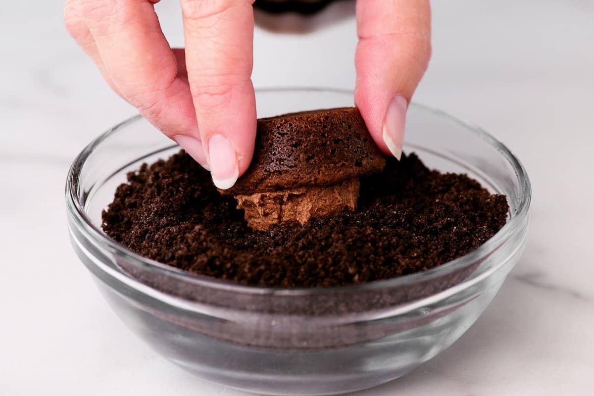 a hand dipping the chocolate cookie cups in oreo cookie crumbs