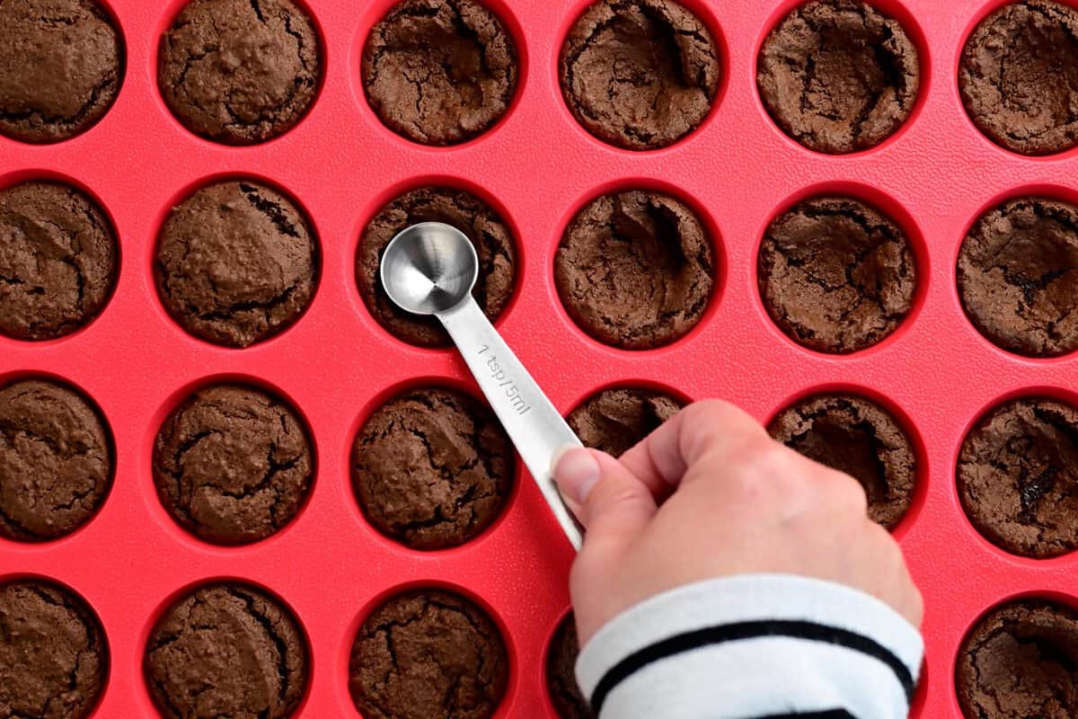 a hand using a teaspoon to make indents in the baked cookie cups