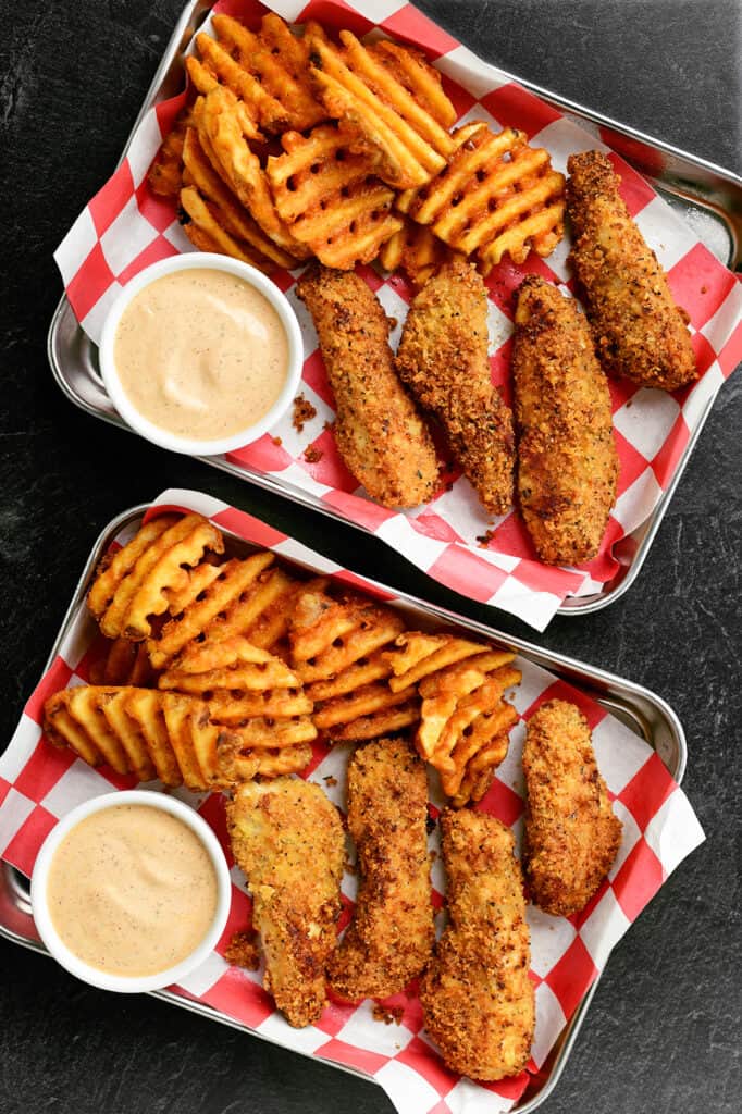 chicken tenders with waffle fries and dipping sauce on trays