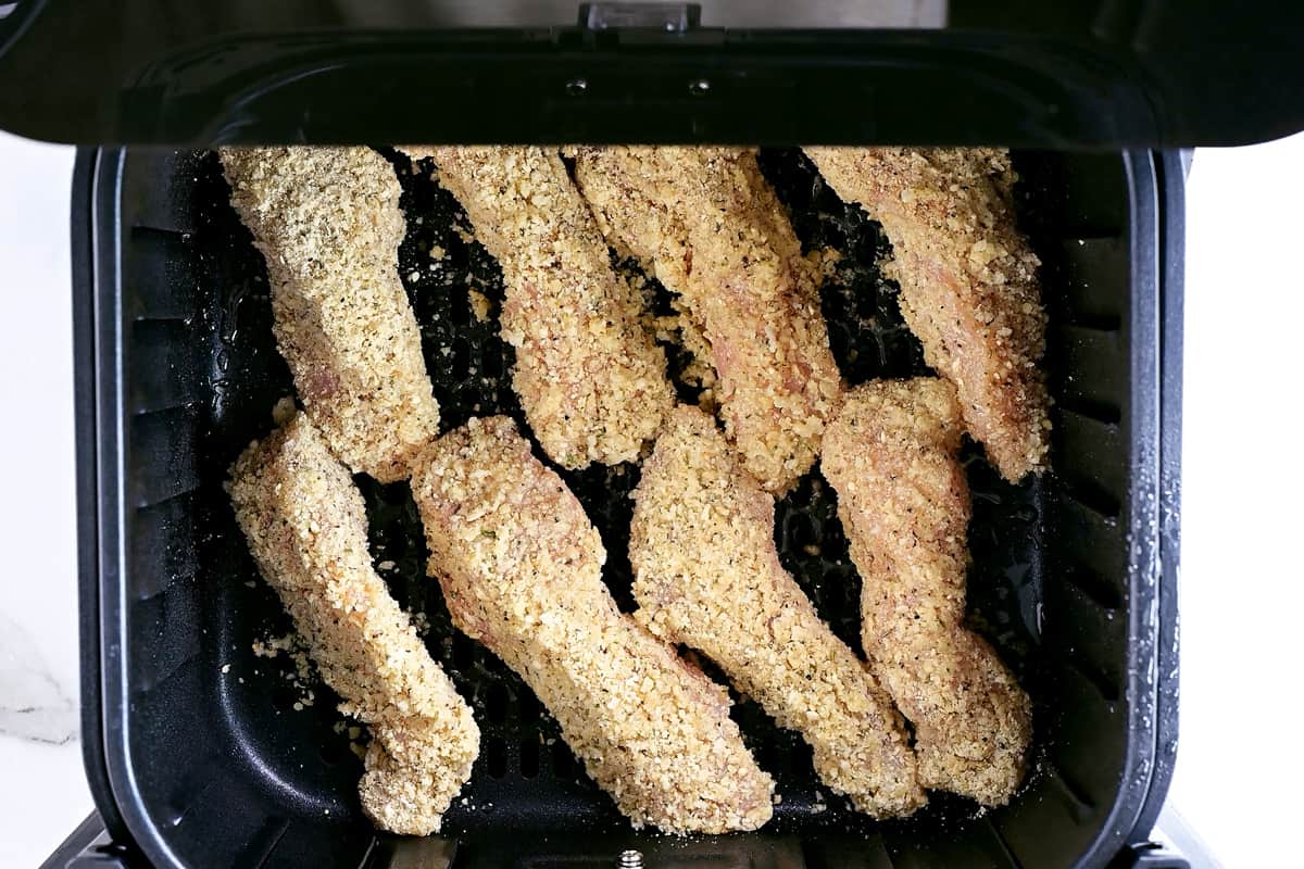eight uncooked chicken tenders in an air fryer basket