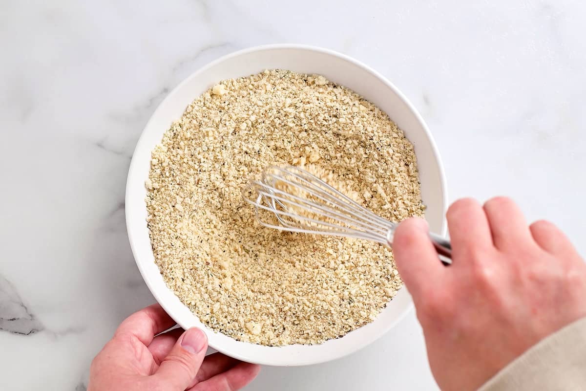 hands use a whisk to stir breading and break up the chunks