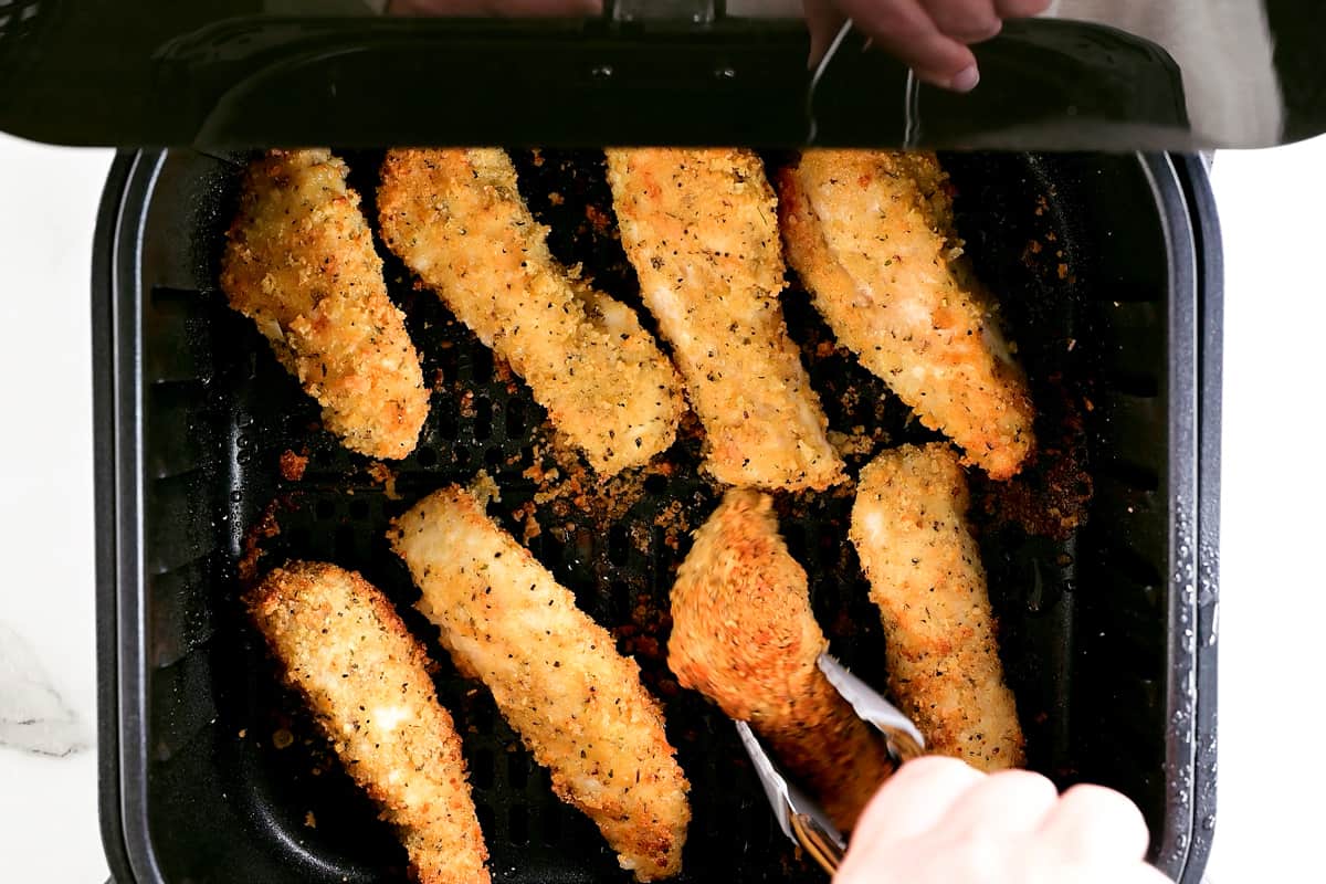 a hand using kitchen tongs to flip the chicken over in the air fryer basket