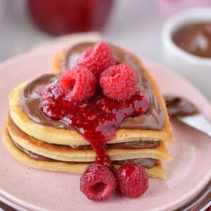 Buttermilk pancakes in a stack with raspberries on top.