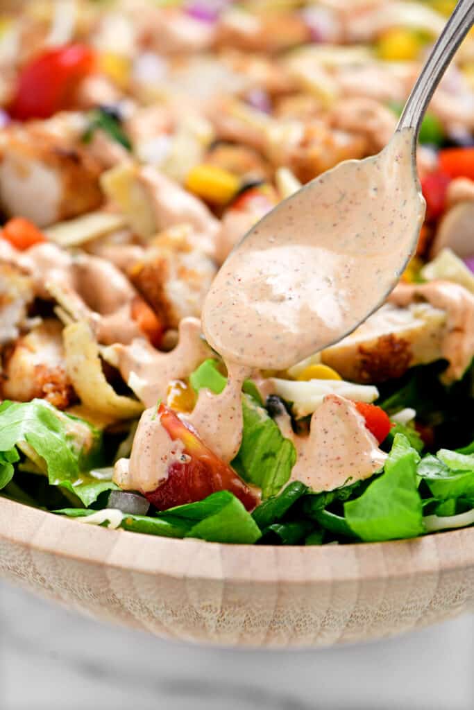 a spoon drizzling dressing onto a salad