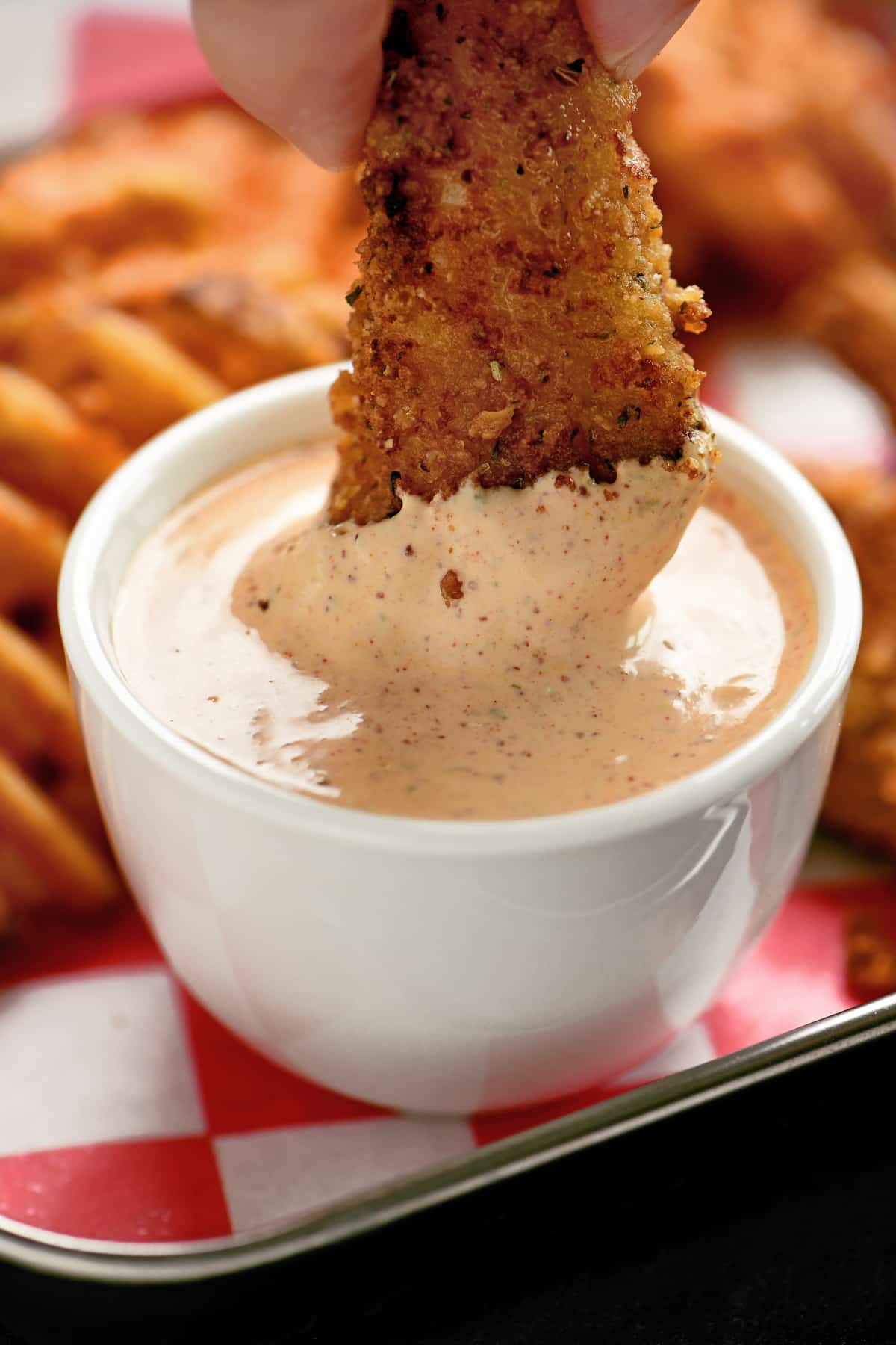 a hand dipping a chicken tender in chipotle ranch dressing