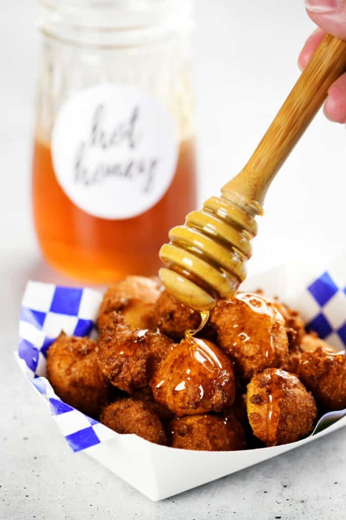 a hand uses a honey wand to drizzle hot honey on hushpuppies
