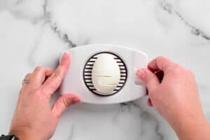 hands using an egg slicer to slice an egg