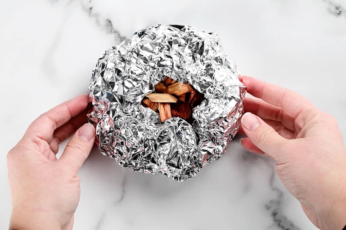 hands forming tinfoil around wood chips