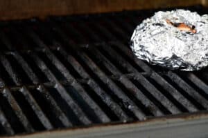 a tinfoil pouch with wood chips on a grill grate