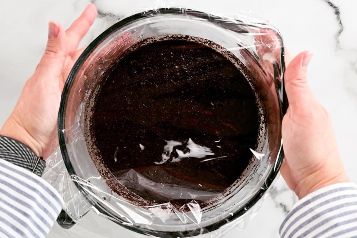 hands adding plastic wrap to a bowl with coffee grounds inside