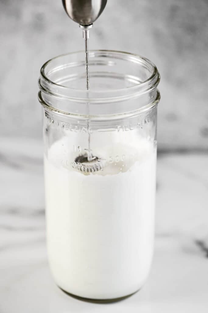 a small hand mixer mixing cold foam in a glass jar