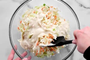 stirring coleslaw dressing into shredded cabbage in a bowl