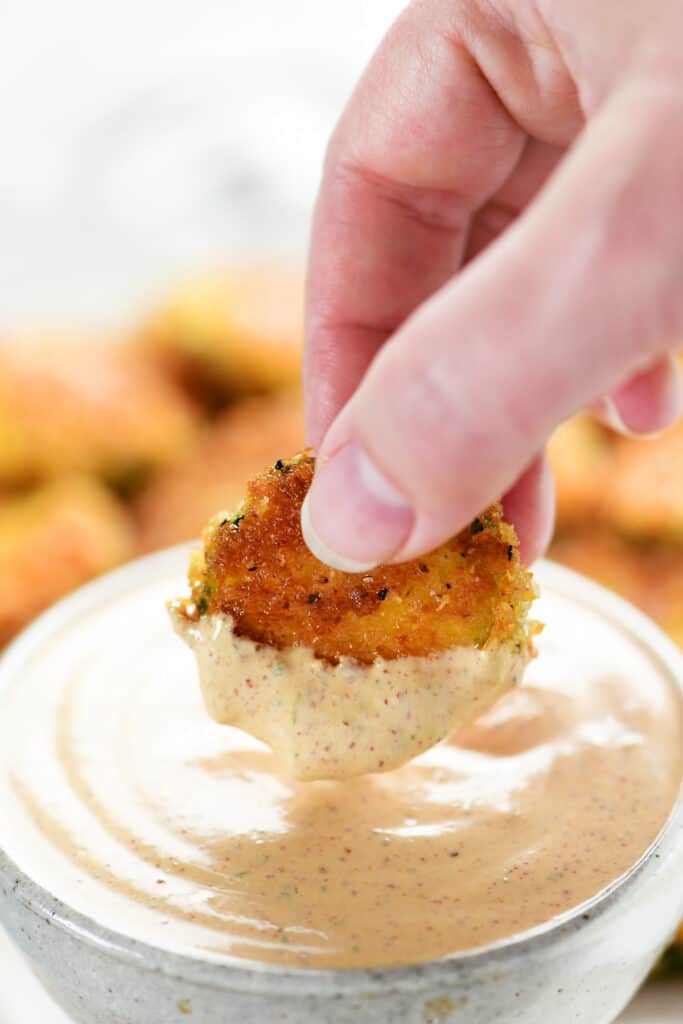 a hand dipping fried zucchini in chipotle ranch