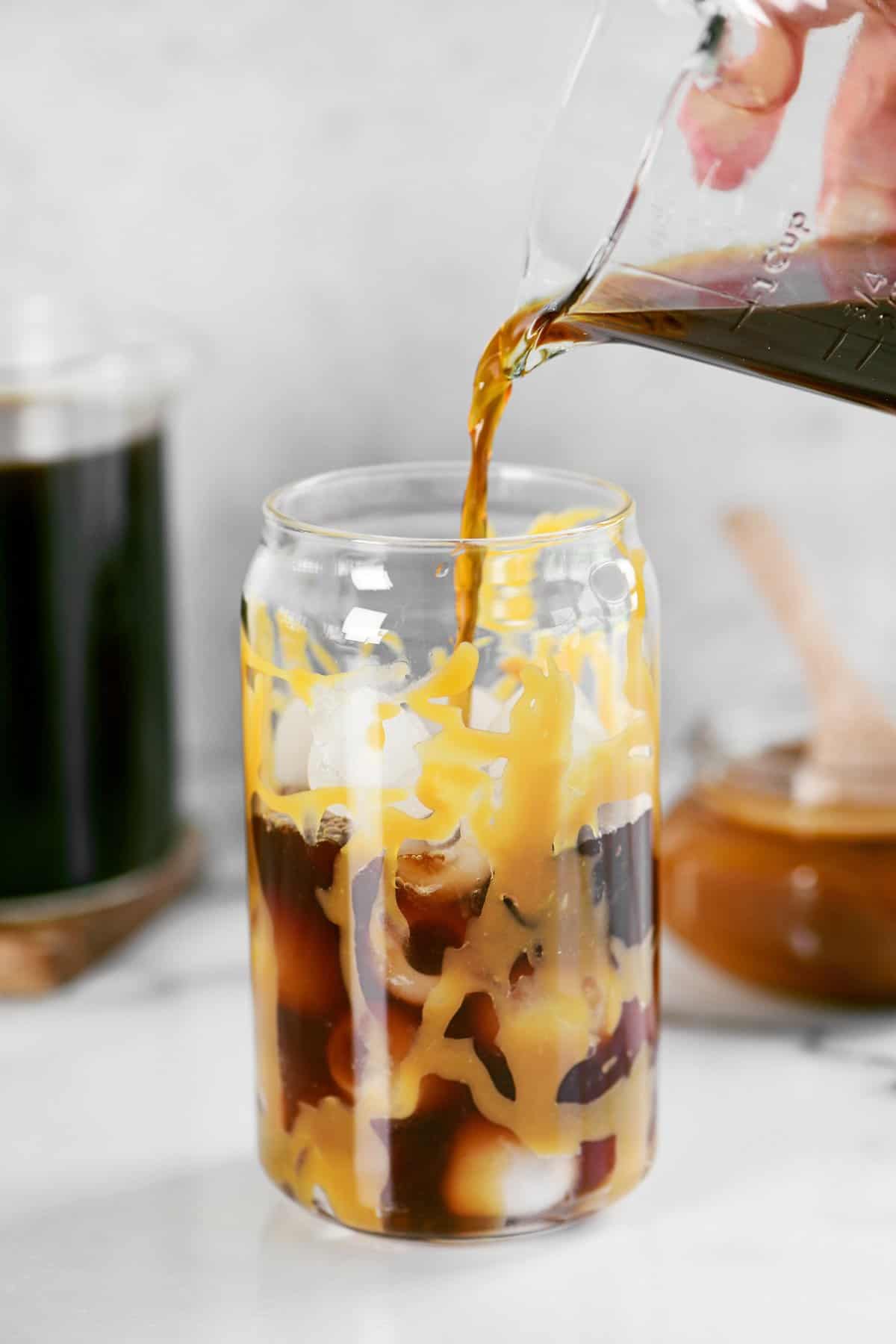 a hand pouring cold brew into a glass with caramel in it.