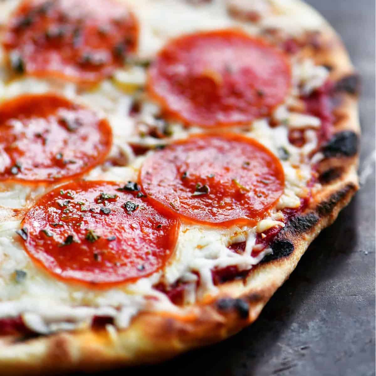 Grilled pepperoni pizza on a black platter.