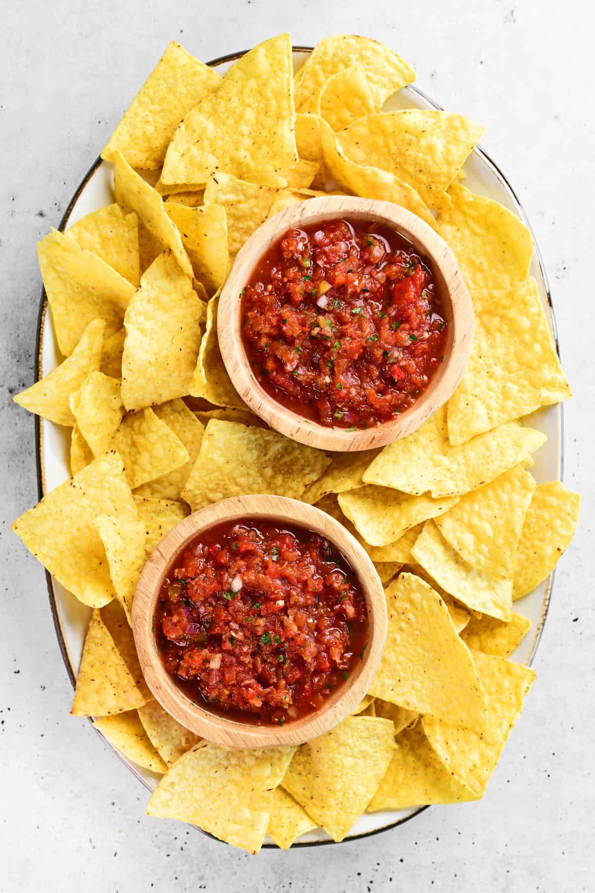 restaurant style salsa in two wooden bowls with tortilla chips on an oval platter
